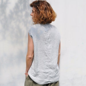 May include: A woman wearing a light blue linen sleeveless top and olive green linen pants. The top has a center back seam.