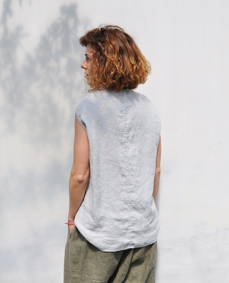 May include: A woman wearing a light blue linen sleeveless top and olive green linen pants. The top has a center back seam.