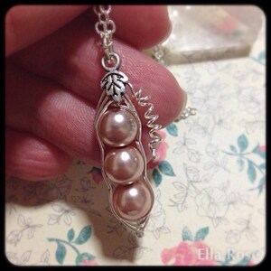 May include: A silver necklace with a charm of three pink pearls in a pea pod. The charm has a silver leaf on top.