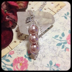 May include: A silver necklace with a charm of three pink pearls in a pea pod shape. The charm is hanging from a silver chain.