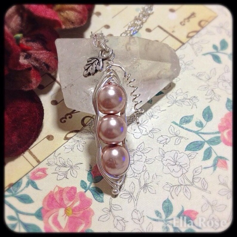 May include: A silver necklace with a charm of three pink pearls in a pea pod shape. The charm is hanging from a silver chain.