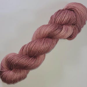 May include: A skein of soft, pink yarn with a subtle shimmer. The yarn is twisted into a loose, rope-like shape.