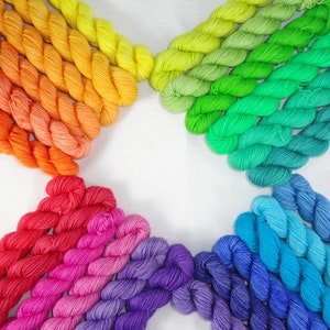 May include: A rainbow of yarn skeins arranged in a star shape on a white background. The yarn is in shades of red, orange, yellow, green, blue, and purple.