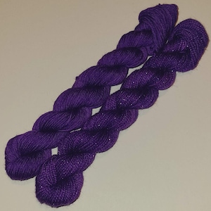 May include: Two skeins of purple yarn, one with a subtle sparkle. The yarn is twisted together and ready for knitting or crocheting.