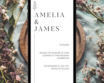 May include: A smartphone displays a wedding invitation with the names "AMELIA & JAMES" in elegant black font. The invitation includes the date "14.09.20XX" and event details. The phone rests on a wooden plate surrounded by floral arrangements.