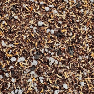 May include: Close-up of a soil mix, featuring a blend of dark brown soil, light-colored perlite, and small pieces of organic matter. The texture is coarse and granular, ideal for gardening and potting plants.