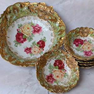 May include: A collection of antique porcelain serving dishes. The set includes a large bowl and several smaller dishes. Each piece features a floral rose design in red, yellow, and pink, with a gold trim and a green border.