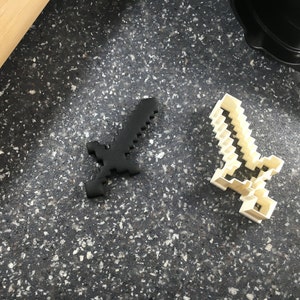 May include: Two cookie cutters shaped like a Minecraft sword. One is black and the other is white.