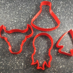 May include: Four red plastic cookie cutters in the shapes of a bull's head, a Christmas tree, a bell, and a ribbon.