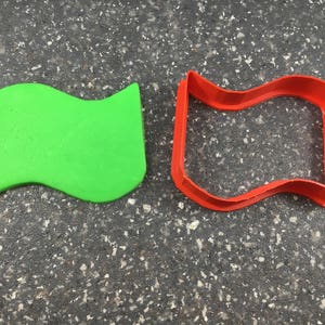 Może przedstawiać: Zielona plastikowa foremka do ciasteczek w kształcie falującej flagi i czerwona plastikowa foremka do ciasteczek w kształcie falującej flagi.