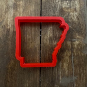 May include: A red plastic cookie cutter shaped like the state of Arkansas.