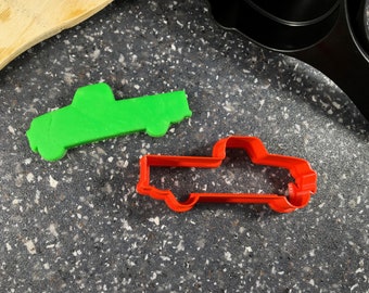 以下が含まれることがあります： ピックアップトラックの形をしたクッキーカッターが2つ。1つは緑色、もう1つは赤色。カッターは灰色の斑点のある表面の上に置かれています。