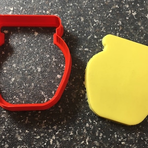 May include: Two cookie cutters in the shape of a jar. The cutter on the left is red and the cutter on the right is yellow.