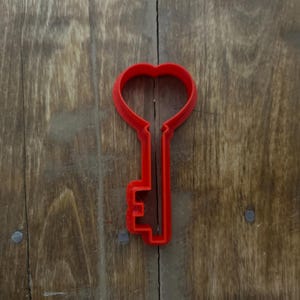 Puede incluir: Cortador de galletas de plástico rojo en forma de llave con una cabeza en forma de corazón.