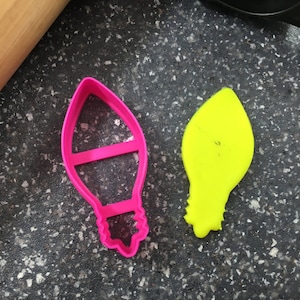 Puede incluir: Dos cortadores de galletas con forma de bombilla. Uno es rosa y el otro es amarillo.