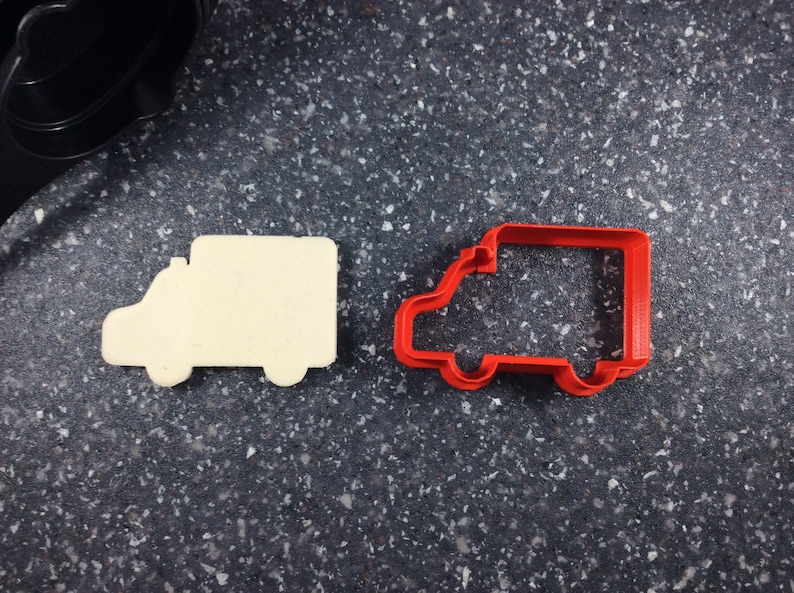 May include: A white cookie cutter shaped like a delivery truck next to a red plastic cookie cutter shaped like a delivery truck.