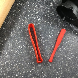 Könnte beinhalten: Zwei rote Plastik-Keksstempel in Form eines Baseballschlägers. Einer ist eine feste Form und der andere ist eine Umrandung.