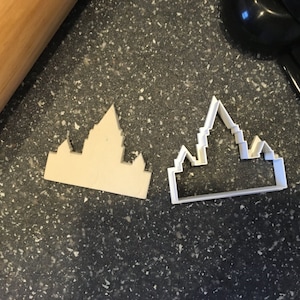 Puede incluir: Dos cortadores de galletas de plástico blanco con forma de castillo. Los cortadores están sobre una superficie gris oscura.