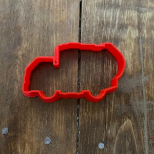Może przedstawiać: Ciastko wykrawacz z czerwonego plastiku w kształcie wywrotki.