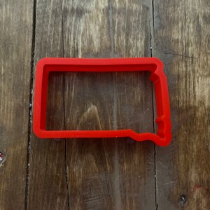 May include: Red plastic cookie cutter shaped like the state of South Dakota.