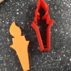 May include: Two cookie cutters in the shape of a torch. One is red and the other is orange.