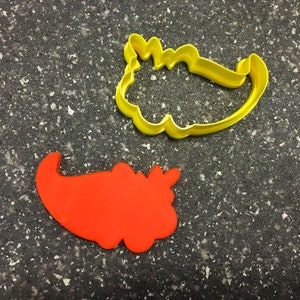 May include: Two cookie cutters, one yellow and one orange, shaped like the Grinch's foot and the Grinch's hat.