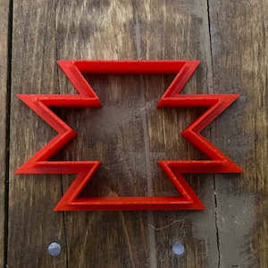 May include: A red plastic cookie cutter shaped like a six-pointed star with a hollow center.