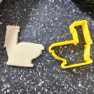 Può includere: Due stampini per biscotti a forma di toilette, uno bianco e uno giallo. Lo stampino bianco è pieno, mentre lo stampino giallo è vuoto.