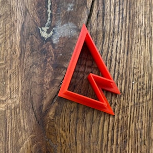 May include: A bright orange plastic cookie cutter shaped like a triangle with a smaller triangle cut out of the center.