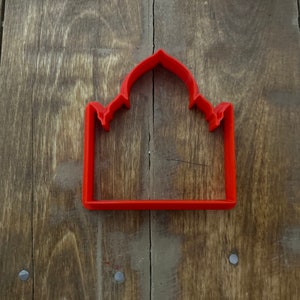 May include: Red plastic cookie cutter shaped like a dome with a rectangular base.