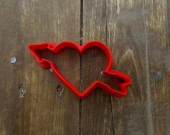 May include: Red plastic cookie cutter shaped like a heart with an arrow through it.