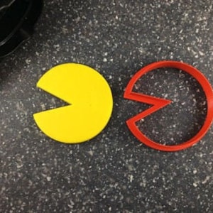 May include: Two cookie cutters, one yellow and one red, shaped like the video game character Pac-Man.