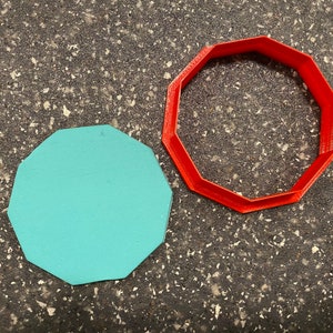 May include: A red octagon-shaped cookie cutter and a turquoise octagon-shaped cookie.