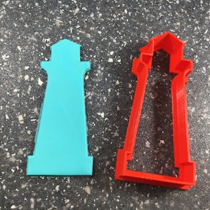 May include: Two lighthouse-shaped cookie cutters. One is solid teal, the other is red with an open center. The cutters are made of plastic and are designed for baking. The lighthouse design is a popular theme for coastal or nautical-themed treats.