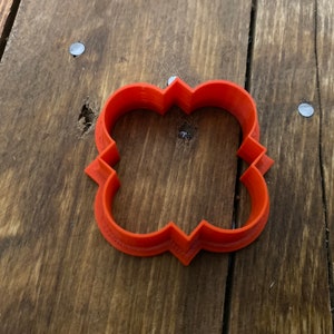May include: Orange plastic cookie cutter shaped like a four-leaf clover with a decorative design.