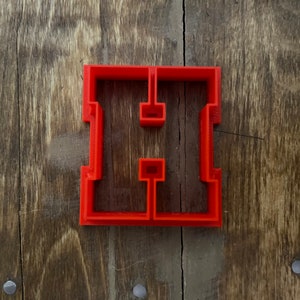May include: Red plastic cookie cutter shaped like the letter "H".