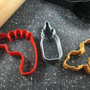 Peut inclure: Trois emportes-pièces, un en forme de biberon, un en forme d'empreinte de pied et un en forme de hochet. L'emporte-pièce biberon est argenté, l'emporte-pièce empreinte de pied est rouge et l'emporte-pièce hochet est doré.