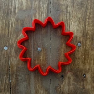 Puede incluir: Cortador de galletas de plástico rojo con forma de sol y borde ondulado.
