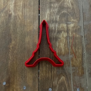 以下が含まれることがあります： 木製の表面に置かれた赤いプラスチック製のエッフェル塔のクッキーカッター