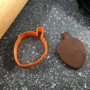 May include: Two acorn-shaped cookie cutters, one orange and one brown. The orange cutter is open and the brown cutter is closed.