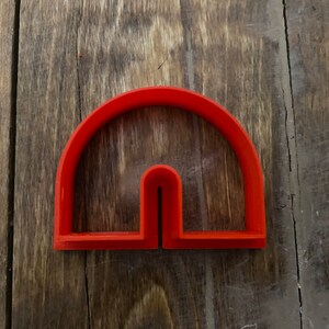 May include: A red plastic cookie cutter shaped like a half circle with a vertical slit in the center.