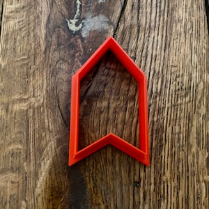 May include: A red plastic cookie cutter shaped like an arrow pointing upwards.