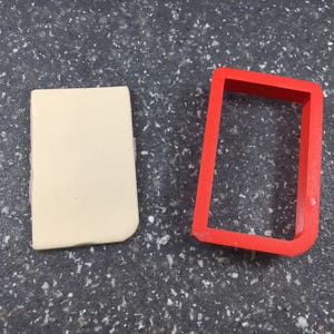 May include: A white rectangular block of fondant next to a red plastic rectangle cookie cutter.