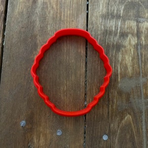 May include: A red plastic cookie cutter shaped like a scalloped circle.