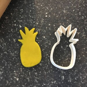 Könnte beinhalten: Ein gelber Ananas-Ausstecher und ein weißer Ananas-Ausstecher aus Kunststoff.