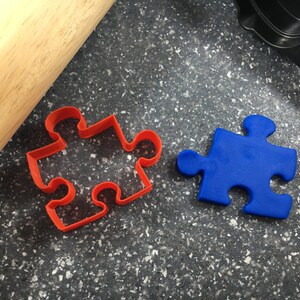 May include: Two puzzle-shaped cookie cutters, one red and one blue, on a dark gray speckled surface.