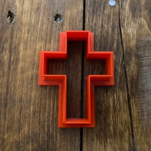 Puede incluir: Un cortador de galletas de plástico rojo con forma de cruz.