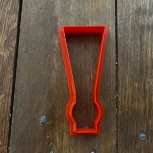 Op de afbeelding: Oranje plastic koekjesvormpje in de vorm van een hoog glas met een afgeronde bodem.