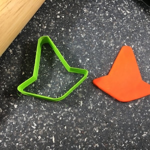 May include: Two cookie cutters, one green and one orange, shaped like traffic cones. The cutters are on a black speckled surface.