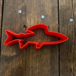 Puede incluir: Un cortador de galletas de plástico rojo en forma de pez.